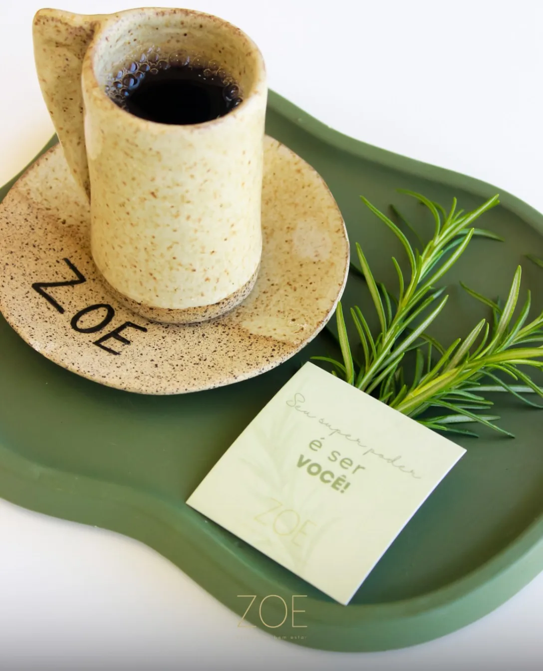 Caneca da ZOE com alecrim sobre a bandeja verde